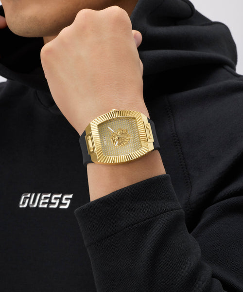 Gold GUESS Mens Black Gold Tone Analog Watch on a wrist with a black hoodie featuring the Guess logo.