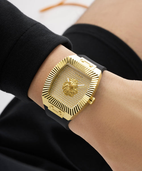 Gold GUESS Mens Black Gold Tone Analog Watch with black strap on a wrist against a neutral background